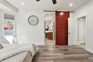 Bedroom featuring light wood-style flooring, a barn door, recessed lighting, connected bathroom, and ceiling fan