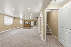 Below grade area with recessed lighting, light carpet, stairs, and freestanding refrigerator