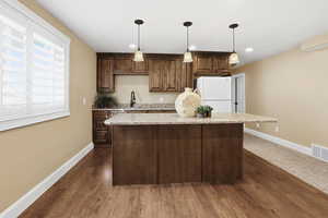 Kitchen with light stone counters, freestanding refrigerator, a kitchen island, hanging light fixtures, and recessed lighting