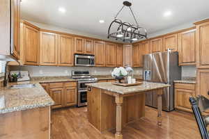 Kitchen featuring appliances with stainless steel finishes, dark wood-type flooring, a breakfast bar area, light stone counters, and recessed lighting