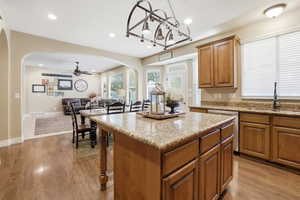 Kitchen featuring arched walkways, brown cabinets, a center island, light stone counters, and open floor plan