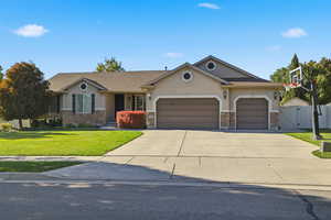 View of front of home with stucco siding, stone siding, a front yard, driveway, and a garage