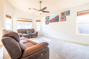 Living room with healthy amount of natural light, ceiling fan, carpet flooring, and lofted ceiling