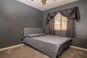 Bedroom with carpet flooring, a textured wall, a ceiling fan, and a textured ceiling