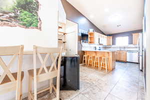 Kitchen with lofted ceiling, open shelves, light brown cabinets, decorative backsplash, and a peninsula