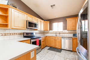 Kitchen featuring appliances with stainless steel finishes, lofted ceiling, open shelves, light tile patterned floors, and tasteful backsplash