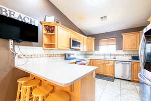 Kitchen with a textured wall, a peninsula, vaulted ceiling, a kitchen breakfast bar, and stainless steel appliances