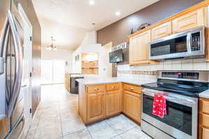 Kitchen with appliances with stainless steel finishes, light countertops, a peninsula, decorative backsplash, and a chandelier