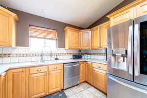 Kitchen featuring stainless steel appliances, light countertops, backsplash, light tile patterned floors, and lofted ceiling