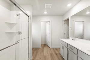 Bathroom with double vanity, light wood-style flooring, a shower stall, and recessed lighting