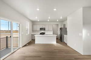 Kitchen featuring appliances with stainless steel finishes, an island with sink, recessed lighting, light wood finished floors, and white cabinets