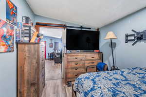 Bedroom with vaulted ceiling, light wood-type flooring, and a barn door