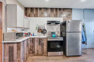 Kitchen featuring appliances with stainless steel finishes, wooden walls, light countertops, light wood finished floors, and extractor fan