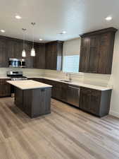 Kitchen featuring dark brown cabinets, a textured ceiling, pendant lighting, appliances with stainless steel finishes, and light wood-style flooring