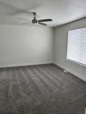 Empty room featuring dark carpet, a textured ceiling, and a ceiling fan