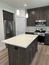 Kitchen featuring dark brown cabinets, stainless steel appliances, a center island, light stone countertops, and recessed lighting