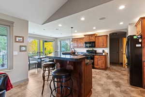 Kitchen with a kitchen island with sink, black appliances, a breakfast bar area, arched walkways, and pendant lighting