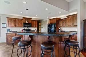 Kitchen featuring a kitchen breakfast bar, recessed lighting, black appliances, decorative light fixtures, and brown cabinetry