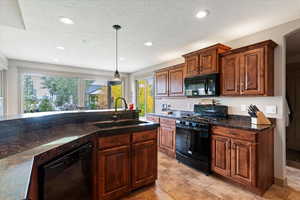 Kitchen with black appliances, a textured ceiling, pendant lighting, dark stone counters, and recessed lighting