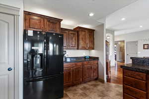 Kitchen with black fridge with ice dispenser, recessed lighting, dark stone countertops, a textured ceiling, and dark brown cabinets