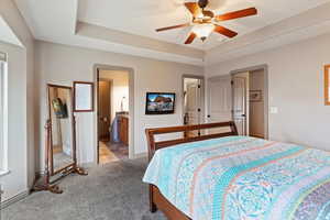 Carpeted bedroom with a raised ceiling, a ceiling fan, and ensuite bathroom