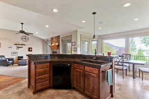 Kitchen featuring vaulted ceiling, a center island with sink, dark countertops, dishwasher, and open floor plan