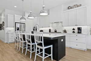 Kitchen with a center island with sink, white cabinets, pendant lighting, tasteful backsplash, and a kitchen bar