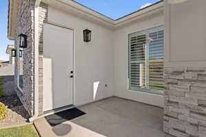 View of exterior entry featuring stone siding, stucco siding, and a patio area