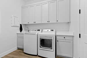 Laundry area featuring light wood-style floors, cabinet space, washer and dryer, and electric panel