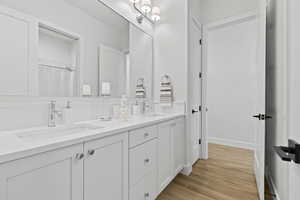 Full bathroom with double vanity, light wood-type flooring, and curtained shower