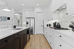 Kitchen featuring white cabinets, pendant lighting, light wood-style flooring, appliances with stainless steel finishes, and tasteful backsplash
