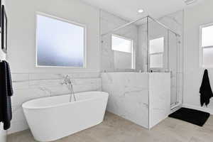 Full bath featuring a soaking tub, a marble finish shower, and tile walls