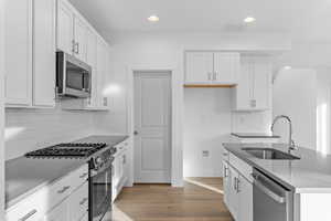 Kitchen with stainless steel appliances, recessed lighting, white cabinets, light wood finished floors, and a center island with sink