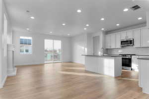 Kitchen with a kitchen island with sink, white cabinets, stainless steel appliances, backsplash, and recessed lighting