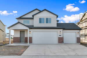 View of front facade featuring brick siding, concrete driveway, a shingled roof, board and batten siding, and an attached garage