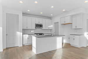 Kitchen with white cabinetry, stainless steel appliances, light wood-style flooring, a center island with sink, and recessed lighting