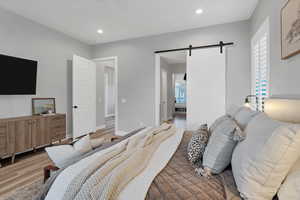 Bedroom featuring a barn door, wood finished floors, recessed lighting, ceiling fan, and ensuite bathroom