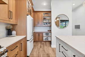 Kitchen with high end white refrigerator, open shelves, light stone counters, light wood-style floors, and recessed lighting