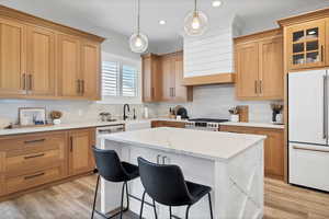 Kitchen featuring a breakfast bar, white built in refrigerator, decorative light fixtures, light stone countertops, and light wood-style floors