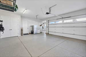 Garage featuring freestanding refrigerator, white refrigerator, and a garage door opener