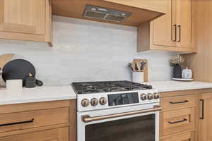 Kitchen featuring white gas range, backsplash, extractor fan, and light brown cabinetry