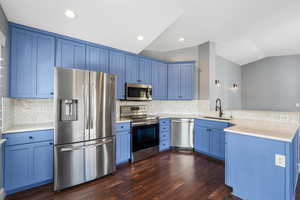 Kitchen with stainless steel appliances, lofted ceiling, blue cabinets, dark wood-type flooring, and a peninsula