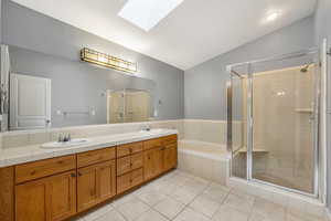 Full bathroom featuring a skylight, a shower stall, double vanity, light tile floors, and a bath