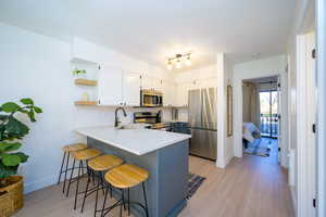 Kitchen with open shelves, appliances with stainless steel finishes, a breakfast bar area, a peninsula, and decorative backsplash