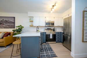 Kitchen with open shelves, appliances with stainless steel finishes, white cabinets, a kitchen breakfast bar, and tasteful backsplash