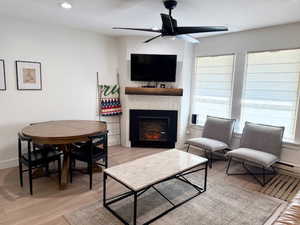 Living area with a fireplace, light LVP floors, a ceiling fan, recessed lighting, and a baseboard radiator