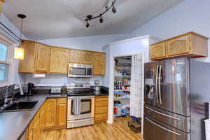 Kitchen featuring stainless steel appliances, dark countertops, pendant lighting, light wood finished floors, and a textured ceiling