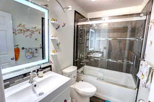 Full bathroom with vanity, enclosed tub / shower combo, and a textured ceiling