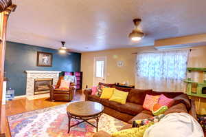 Living area featuring wood finished floors, a textured ceiling, a stone fireplace, and ceiling fan