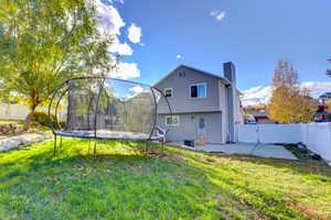 Rear view of property featuring a fenced backyard, a trampoline, a chimney, and a patio